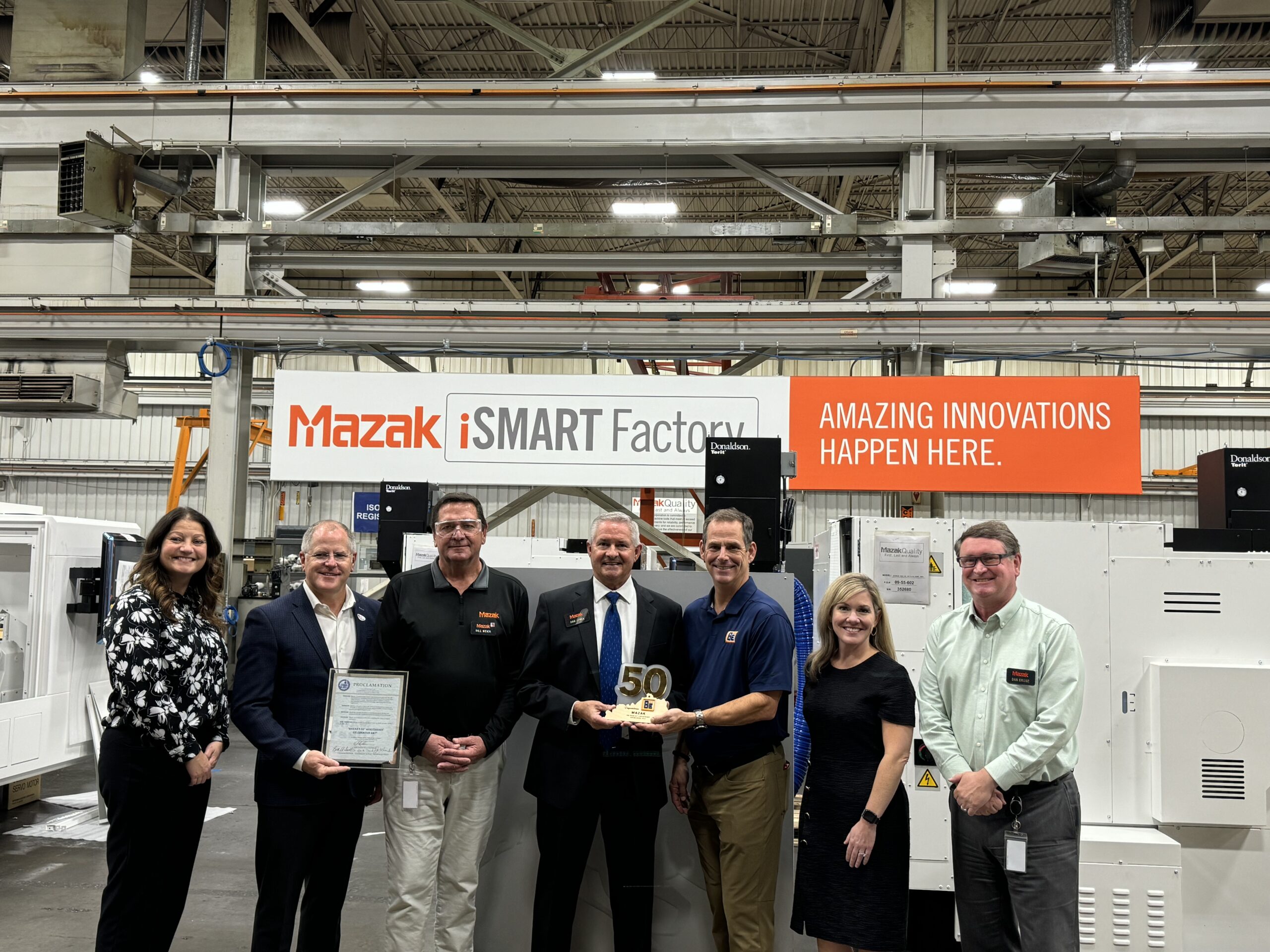 Mazak President Dan Janka stands in the middle of a group of people while holding a 50th anniversary award